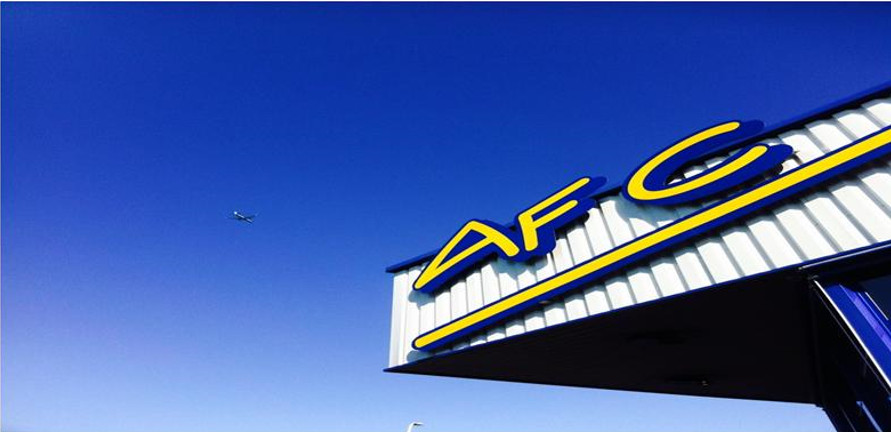 Enseigne du magasin AFC 14 à Caen, spécialiste des stores bannes et portails. Lettrage AFG bleu et jaune sur tôle ondulée blanche.